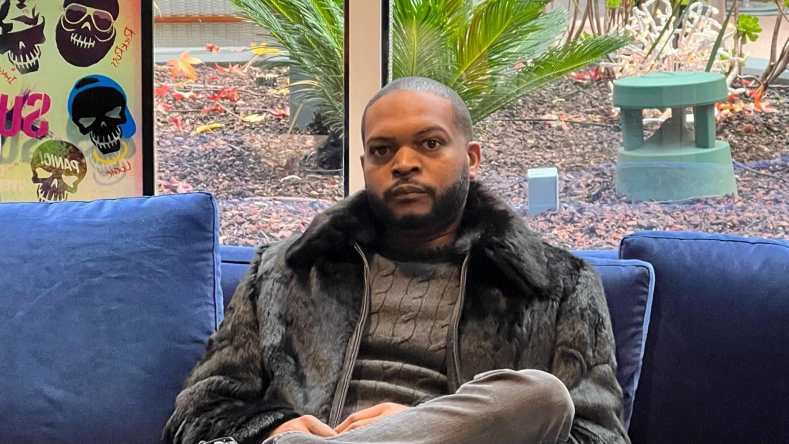 特里克·沃克(Terique Walker)穿着黑色毛皮大衣和高领毛衣坐在蓝色沙发上.